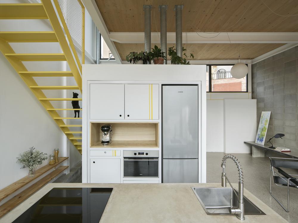 Ett kök sett framifrån och till vänster i bild leder en gul trappa upp till övervåningen