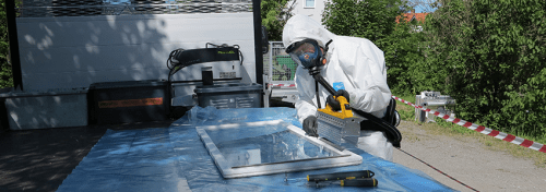 En glasmästare i syddskläder avlägsnar fönsterkitt som innehåller asbest