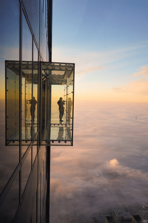 En person står på en balkong helt i glas högt upp på en skyskrapa