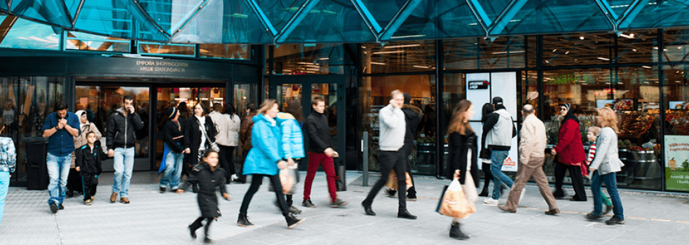 Människor utanför ett köpcentrum som har en stor blå glasfasad